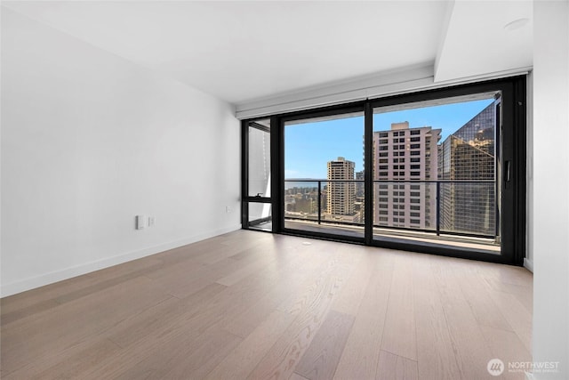 spare room featuring a wall of windows, a view of city, wood finished floors, and baseboards