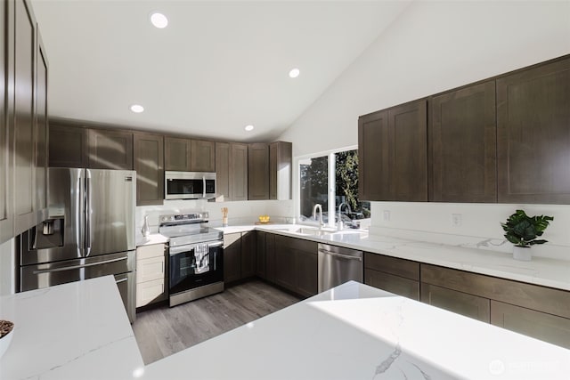 kitchen with stainless steel appliances, dark brown cabinets, a sink, and light wood-style floors