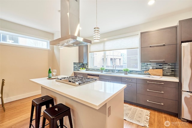 kitchen with a breakfast bar, a sink, light countertops, appliances with stainless steel finishes, and island exhaust hood