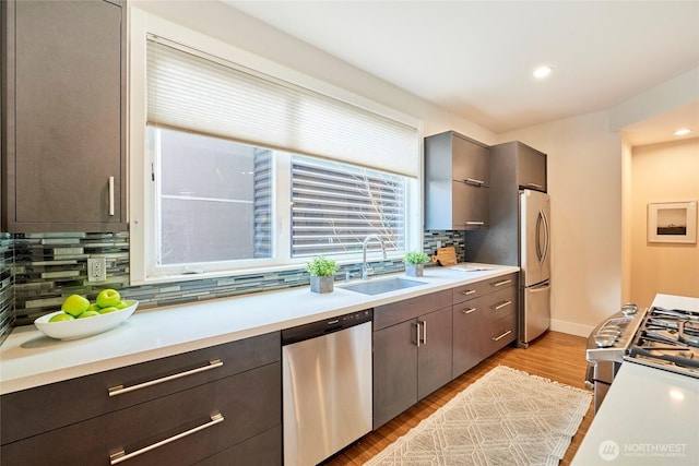 kitchen featuring decorative backsplash, appliances with stainless steel finishes, light countertops, light wood-style floors, and a sink