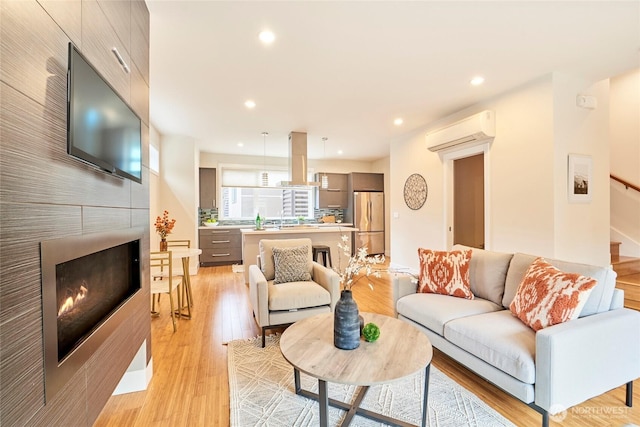 living room featuring a fireplace, recessed lighting, stairway, a wall mounted AC, and light wood-type flooring