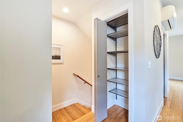 stairs featuring a wall mounted air conditioner, wood finished floors, and baseboards