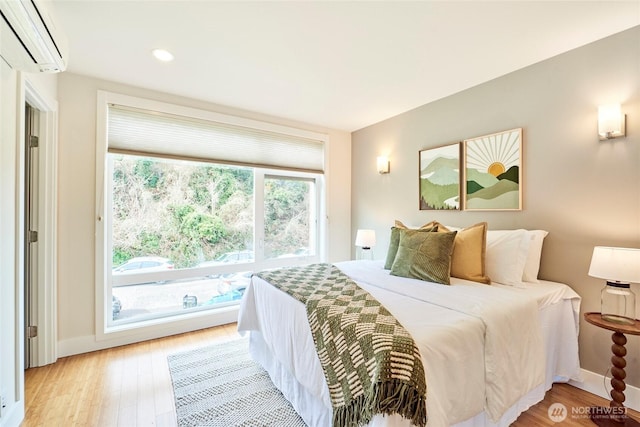 bedroom featuring a wall unit AC, light wood-type flooring, baseboards, and recessed lighting