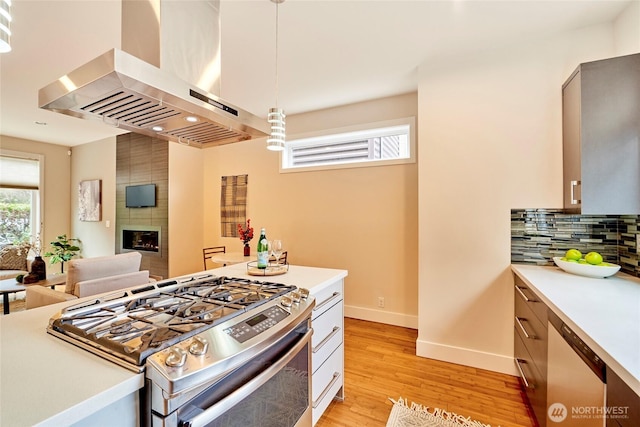 kitchen with light countertops, a large fireplace, wall chimney range hood, stainless steel gas range oven, and dishwashing machine