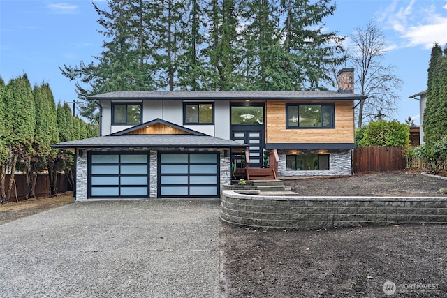 view of front of property with stone siding, a chimney, fence, and driveway