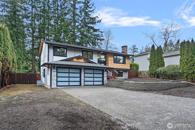 view of front facade with stone siding, driveway, a chimney, and fence