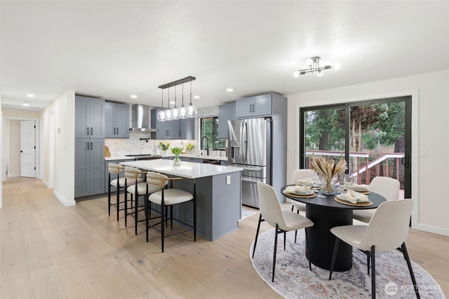 kitchen with a sink, light countertops, a center island, wall chimney exhaust hood, and stainless steel fridge