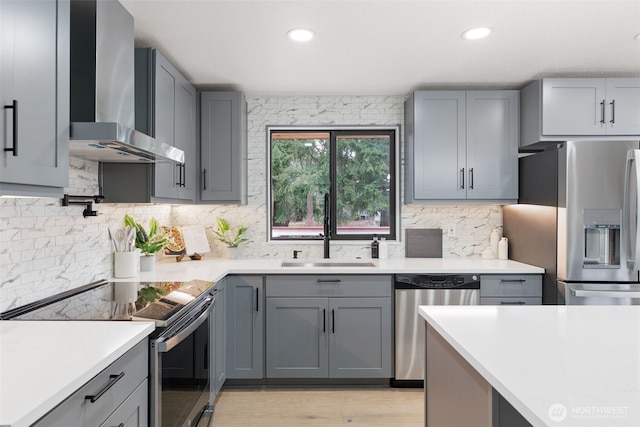 kitchen with stainless steel appliances, wall chimney range hood, light countertops, and gray cabinetry