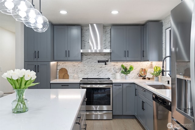 kitchen with stainless steel appliances, light countertops, a sink, and wall chimney exhaust hood