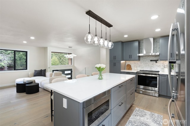 kitchen featuring light countertops, appliances with stainless steel finishes, gray cabinets, decorative backsplash, and wall chimney exhaust hood