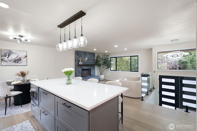 kitchen with light wood-style flooring, stainless steel microwave, a center island, gray cabinetry, and a fireplace