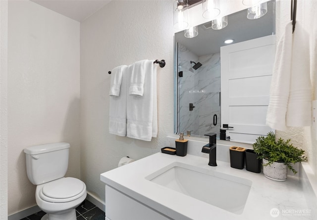 full bath featuring a marble finish shower, a textured wall, toilet, vanity, and baseboards