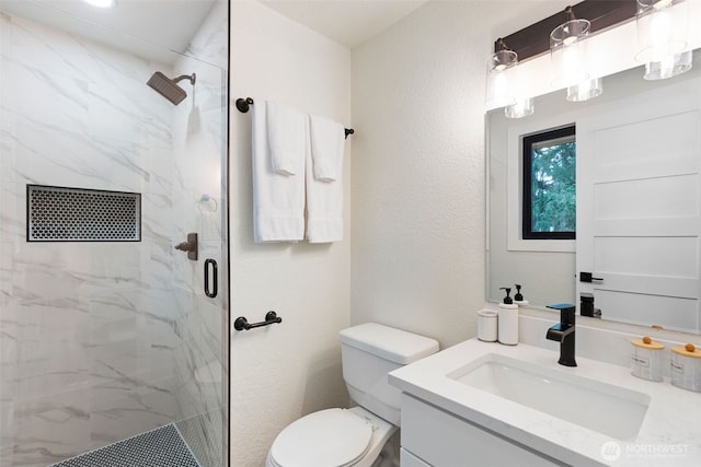 bathroom featuring toilet, a marble finish shower, vanity, and a textured wall