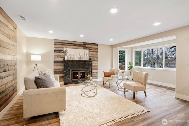 living room with baseboards, visible vents, wood finished floors, a stone fireplace, and recessed lighting