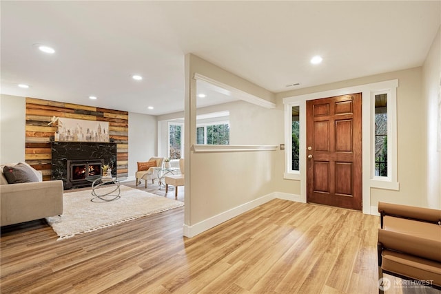 foyer featuring light wood-style floors, a warm lit fireplace, baseboards, and recessed lighting