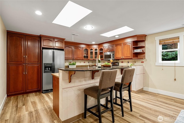 kitchen with a breakfast bar area, appliances with stainless steel finishes, light wood-type flooring, open shelves, and glass insert cabinets