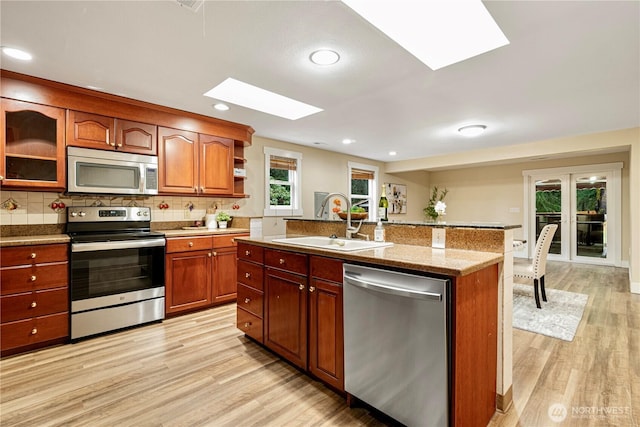 kitchen featuring light wood-style floors, appliances with stainless steel finishes, decorative backsplash, and a sink