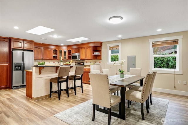 dining area featuring light wood finished floors, a skylight, baseboards, and recessed lighting