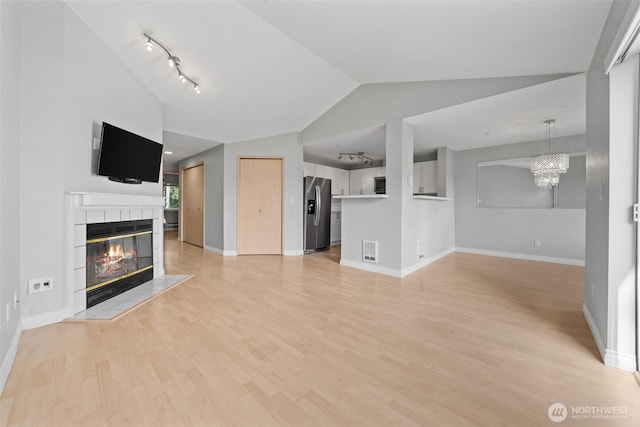 unfurnished living room with baseboards, lofted ceiling, light wood-style floors, a fireplace, and a chandelier