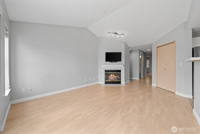 unfurnished living room with light wood-style floors, a tile fireplace, vaulted ceiling, and baseboards