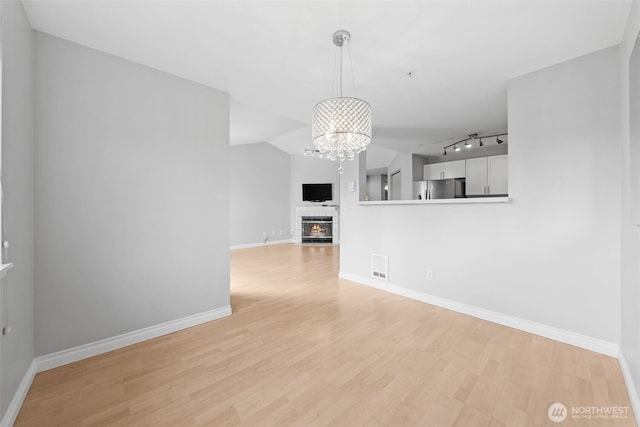 unfurnished living room featuring a notable chandelier, visible vents, light wood-style flooring, a glass covered fireplace, and baseboards