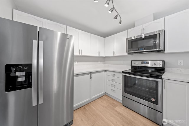 kitchen with light wood finished floors, white cabinetry, stainless steel appliances, and light countertops