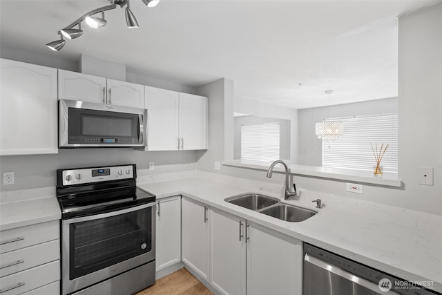 kitchen featuring pendant lighting, stainless steel appliances, light wood-style floors, white cabinetry, and a sink