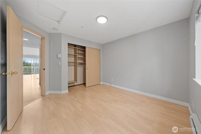 unfurnished bedroom with light wood-type flooring, attic access, baseboards, and a baseboard radiator