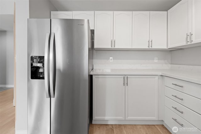 kitchen with light countertops, light wood-style flooring, stainless steel fridge, and white cabinetry