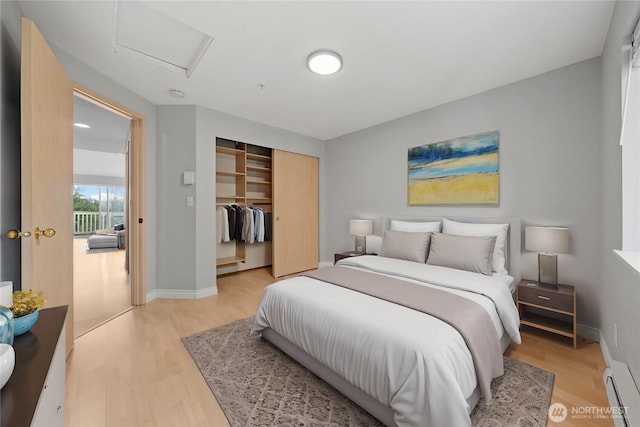 bedroom featuring attic access, baseboards, light wood-style flooring, baseboard heating, and a closet