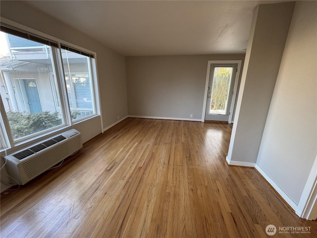 empty room with a wall unit AC, baseboards, and wood finished floors