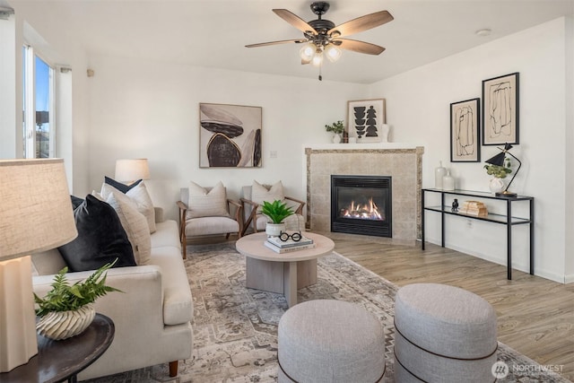 living room with baseboards, a tiled fireplace, a ceiling fan, and wood finished floors