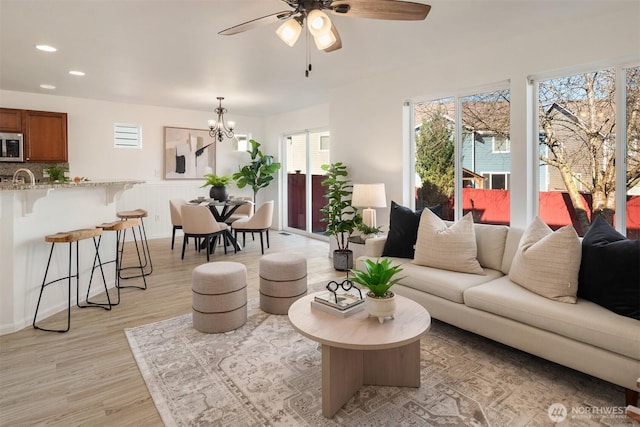 living area with ceiling fan with notable chandelier, light wood-type flooring, and recessed lighting