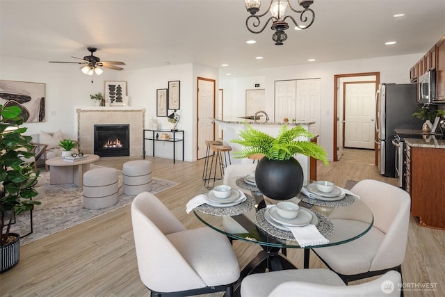 dining space featuring light wood-style floors, a high end fireplace, ceiling fan with notable chandelier, and recessed lighting