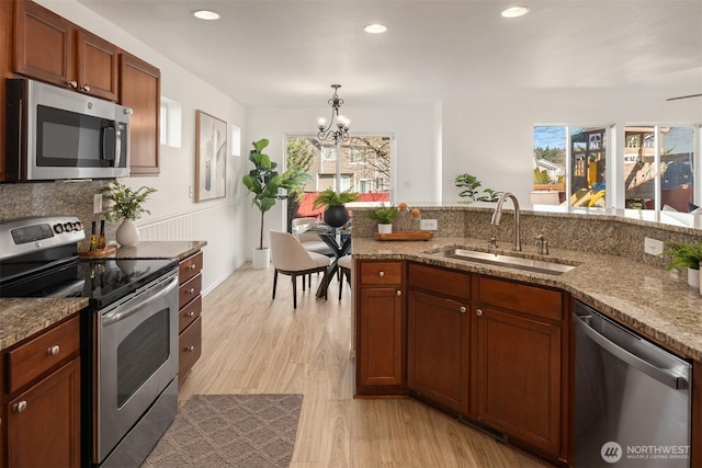 kitchen featuring stone counters, stainless steel appliances, an inviting chandelier, a sink, and light wood-type flooring