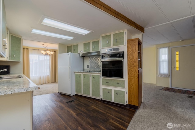 kitchen with wall oven, green cabinetry, freestanding refrigerator, under cabinet range hood, and a sink