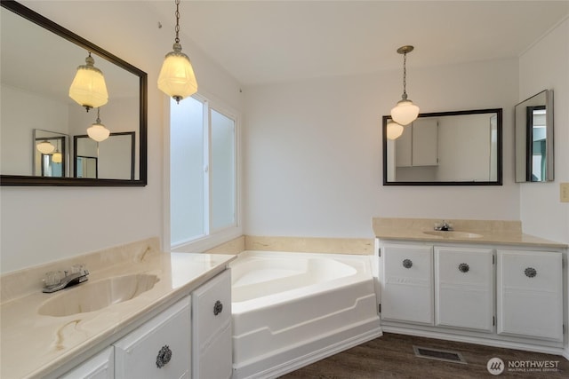 full bath with wood finished floors, two vanities, a sink, visible vents, and a bath