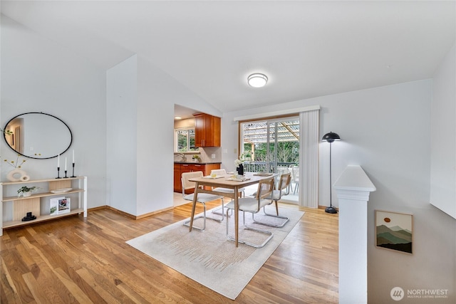 dining area featuring vaulted ceiling, light wood-type flooring, and baseboards