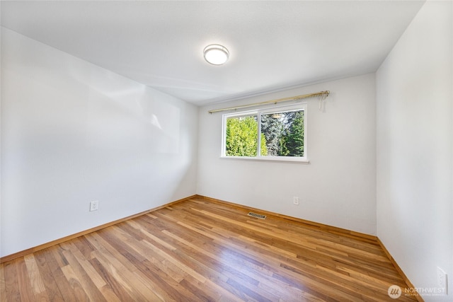 empty room with wood finished floors, visible vents, and baseboards