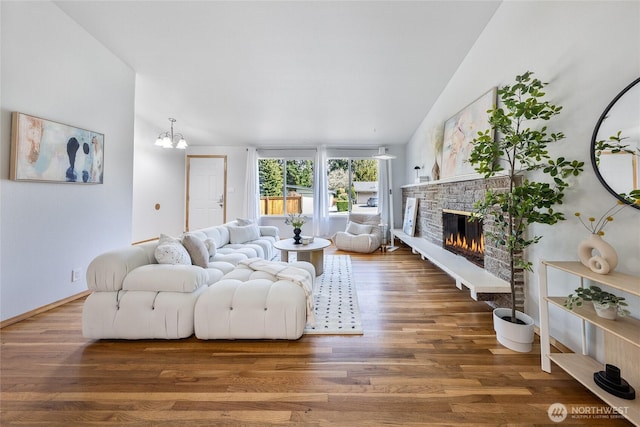 living room featuring an inviting chandelier, a fireplace, baseboards, and wood finished floors