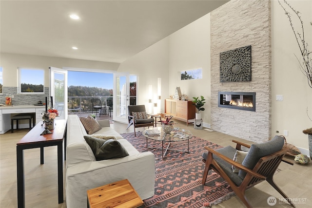 living room featuring baseboards, a stone fireplace, a high ceiling, and recessed lighting