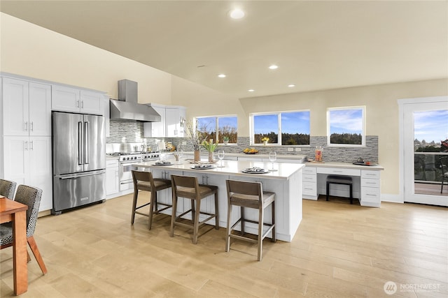 kitchen with high end appliances, wall chimney exhaust hood, a center island, light countertops, and a kitchen bar