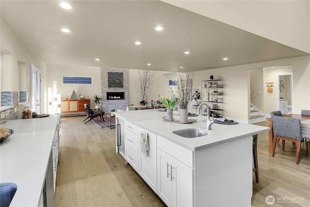 kitchen with light wood finished floors, open floor plan, a sink, and a stone fireplace