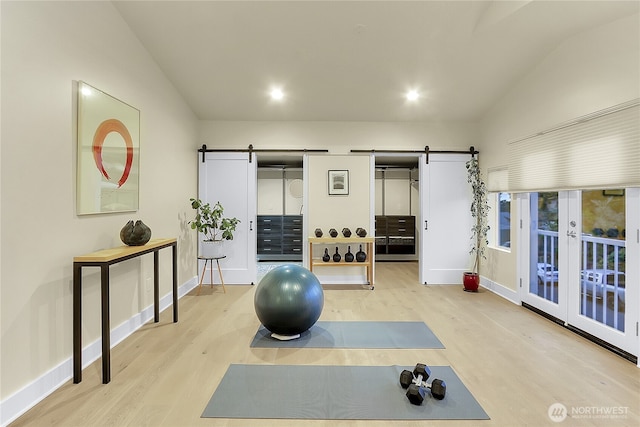 workout area featuring lofted ceiling, wood finished floors, baseboards, and a barn door