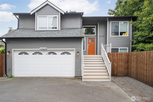 bi-level home featuring driveway, an attached garage, fence, and roof with shingles