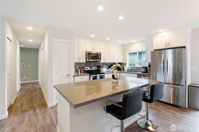 kitchen featuring a center island, white cabinets, appliances with stainless steel finishes, decorative backsplash, and a kitchen bar