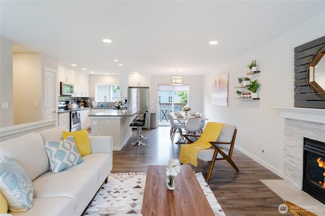 living room with recessed lighting, a stone fireplace, baseboards, and wood finished floors