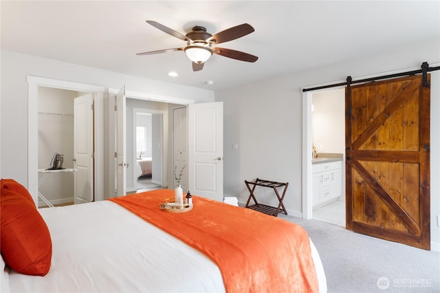 bedroom with a barn door, light colored carpet, a ceiling fan, a closet, and ensuite bath