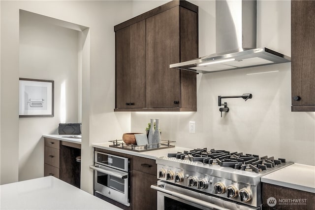 kitchen featuring wall chimney exhaust hood, appliances with stainless steel finishes, light countertops, and dark brown cabinetry