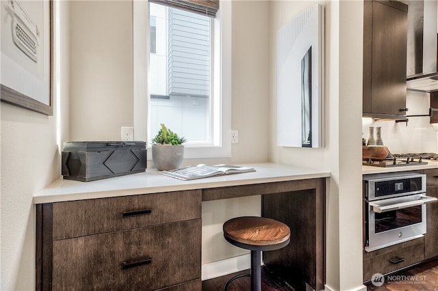 kitchen with light countertops, appliances with stainless steel finishes, wall chimney range hood, dark brown cabinets, and a kitchen breakfast bar